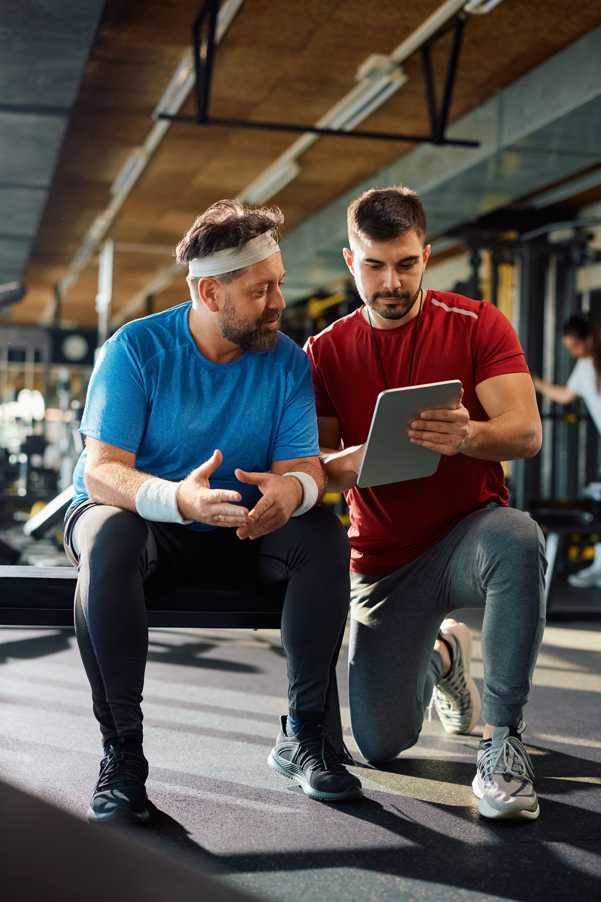 Personal trainer and mature man using digital tablet during gym workout.